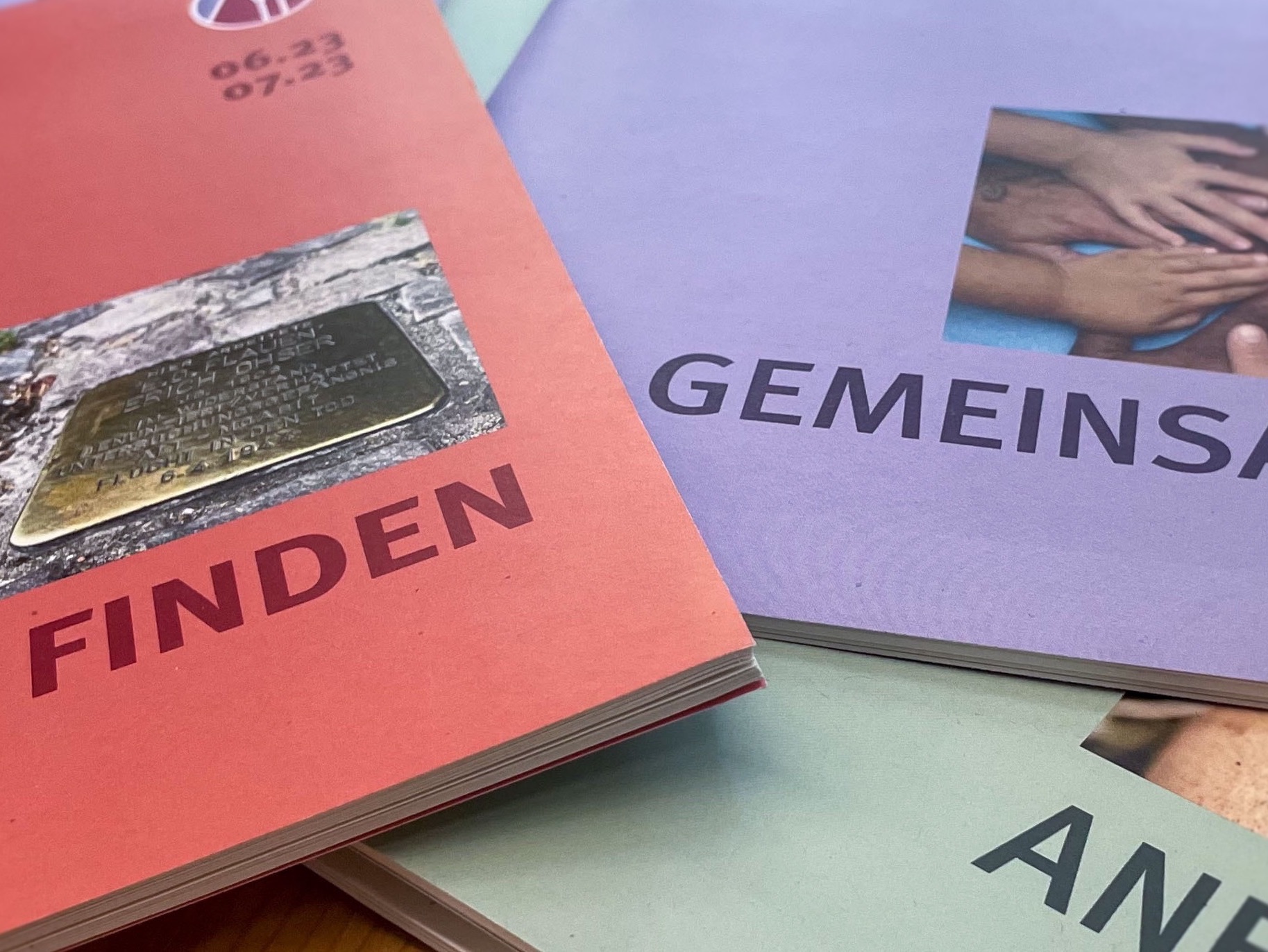 Gedruckte Broschüren mit deutschen Titeln „FINDEN“ und „GEMEINSAM“ gestapelt.