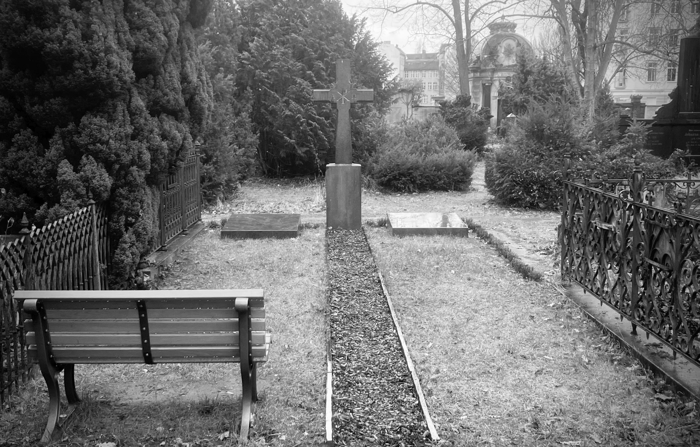Grabsteine, Kreuz und Bänke auf einem monochromen, alten Friedhof.
